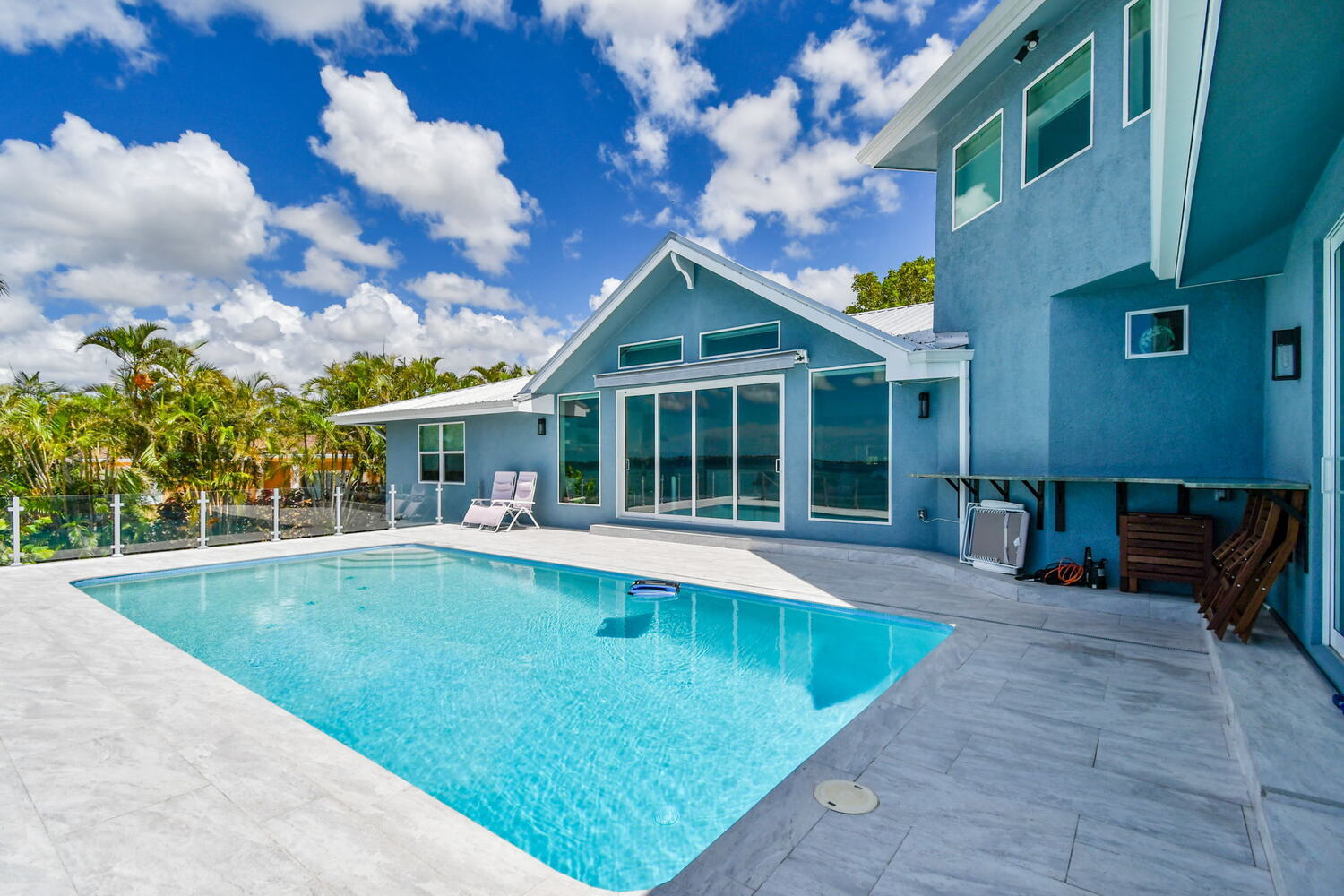 Custom outdoor pool with light stone deck and modern glass railing by Adkins Building & Construction in Bradenton, FL.