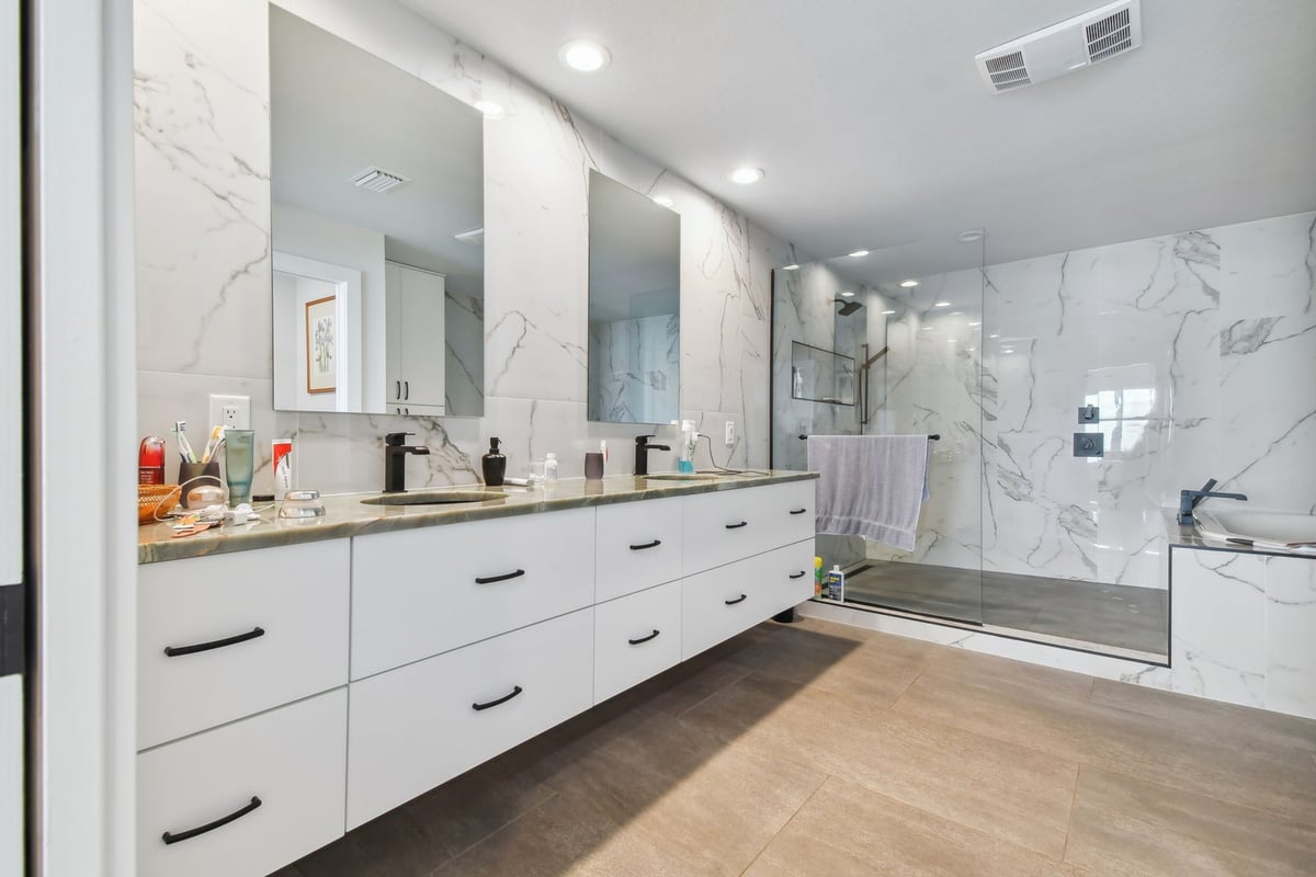 Luxury double vanity bathroom with marble walls and walk-in shower by Adkins Building & Construction in Bradenton, FL.