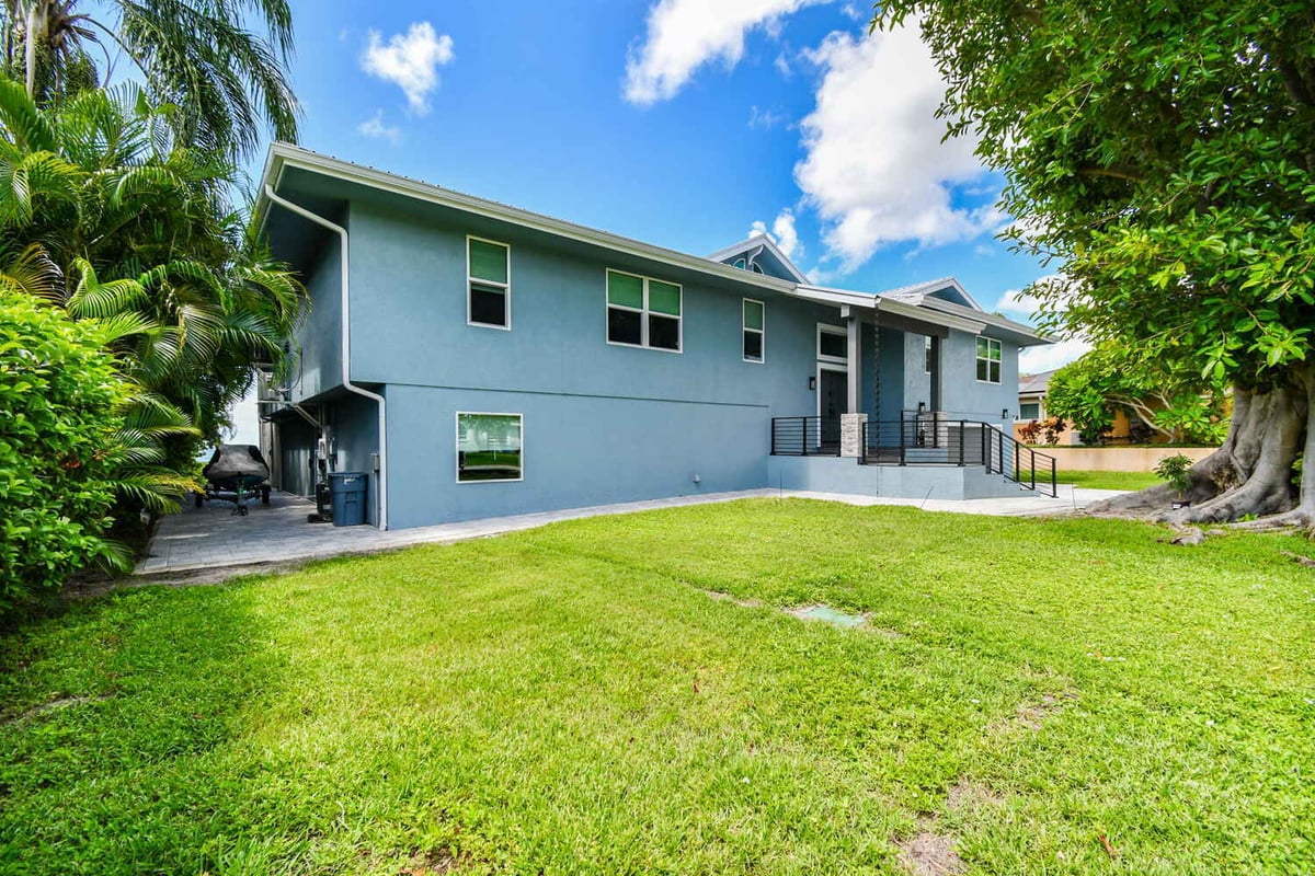 Rear exterior of custom home with blue stucco and modern railing in Bradenton, FL by Adkins Building & Construction.