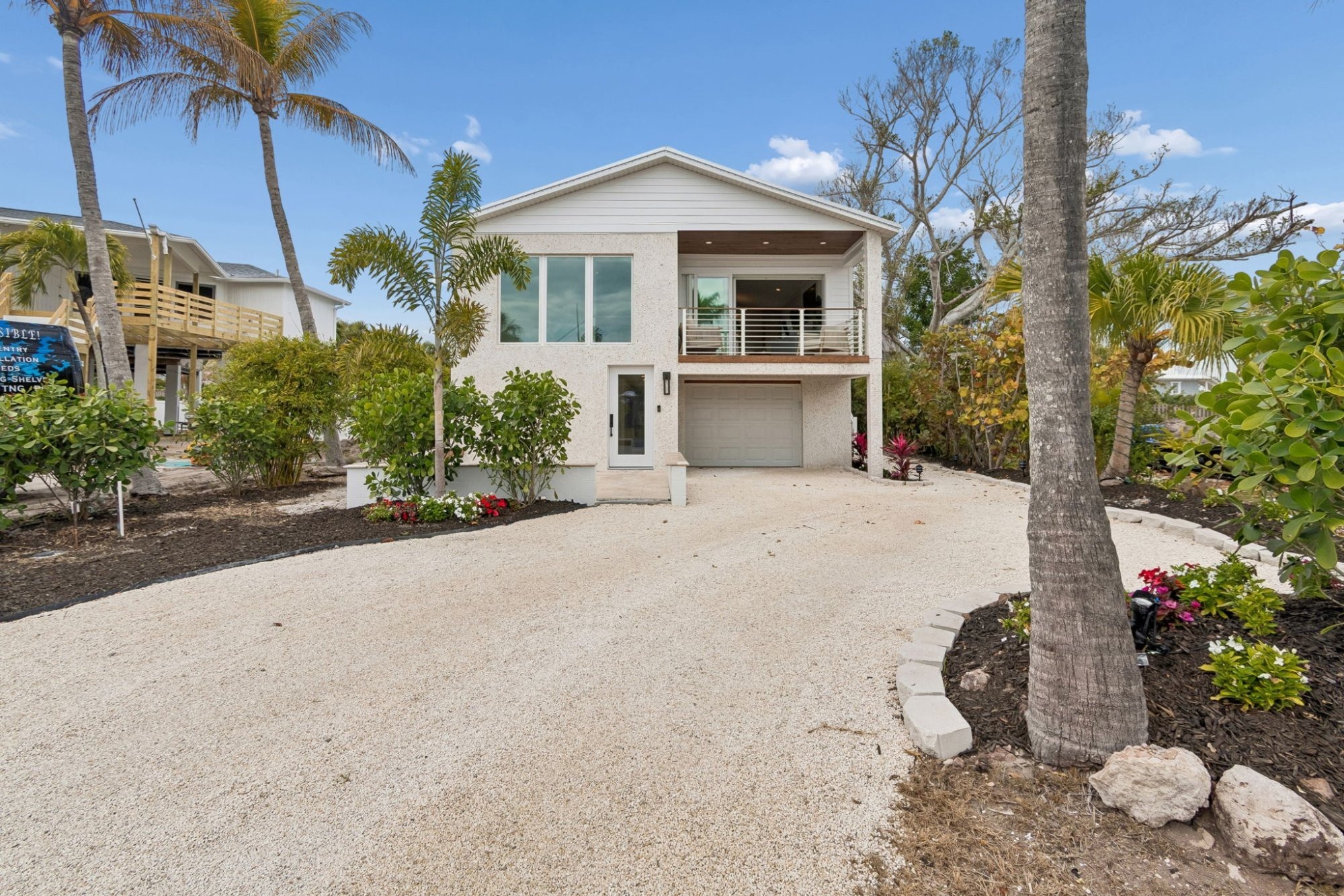 Coastal Home Exterior Daytime Front Facade White Stucco Gravel Driveway Palm Trees