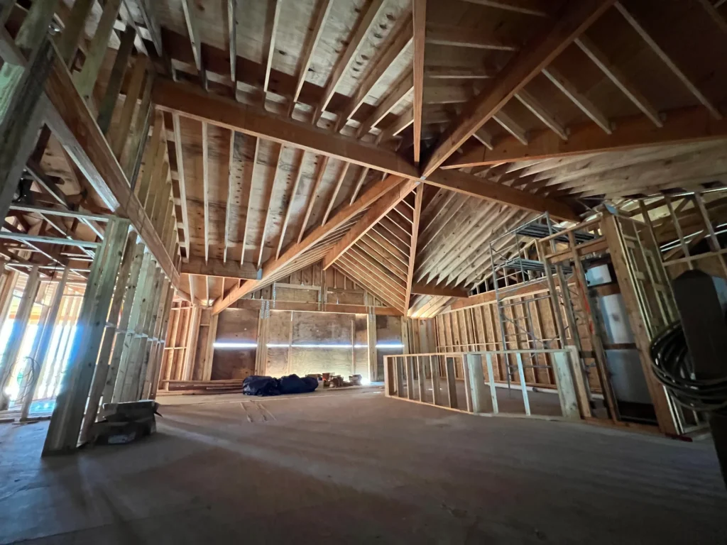 Adkins Building and Construction house project under construction with exposed wood framing, vaulted ceiling trusses, and unfinished interior.
